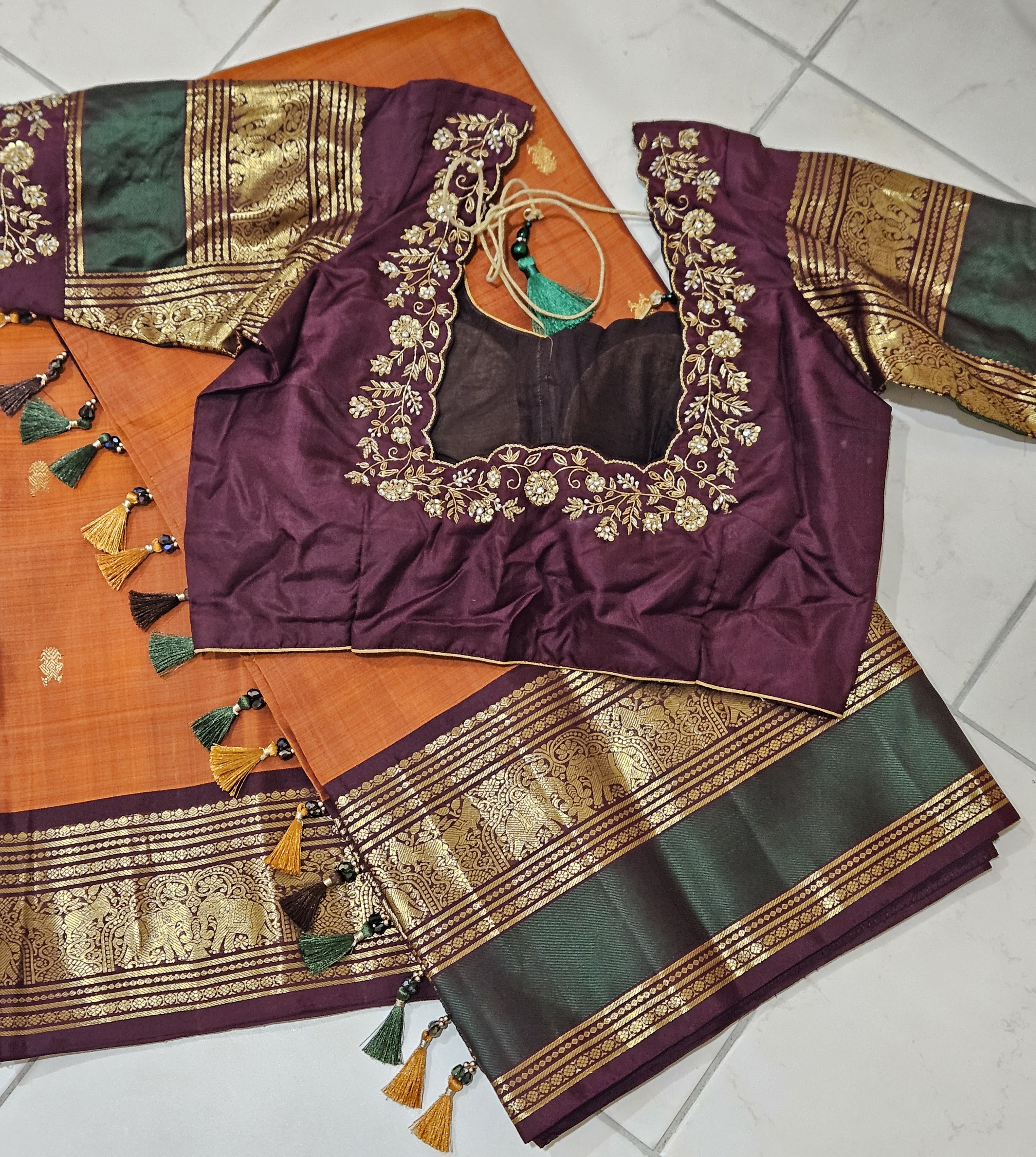 Rust orange and brown pure Kanchipuram silk saree with gold handwoven zari border, paired with a purple embroidered blouse.