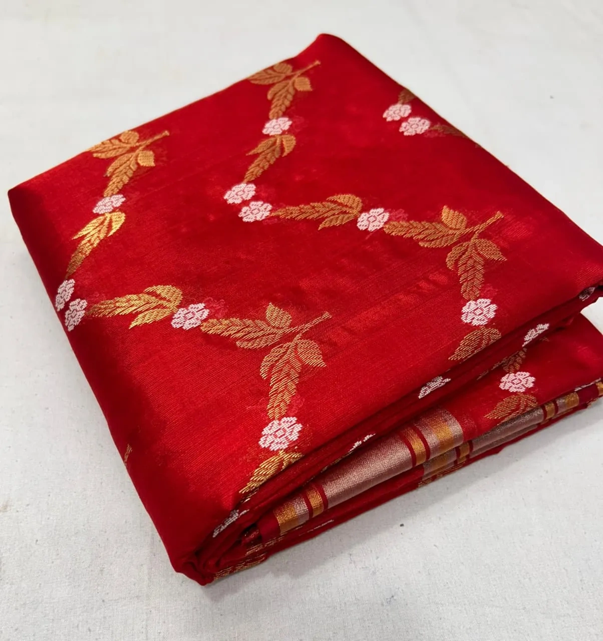 Handwoven red Chanderi silk saree with gold zari floral motifs and delicate pink accents, folded on a plain surface
