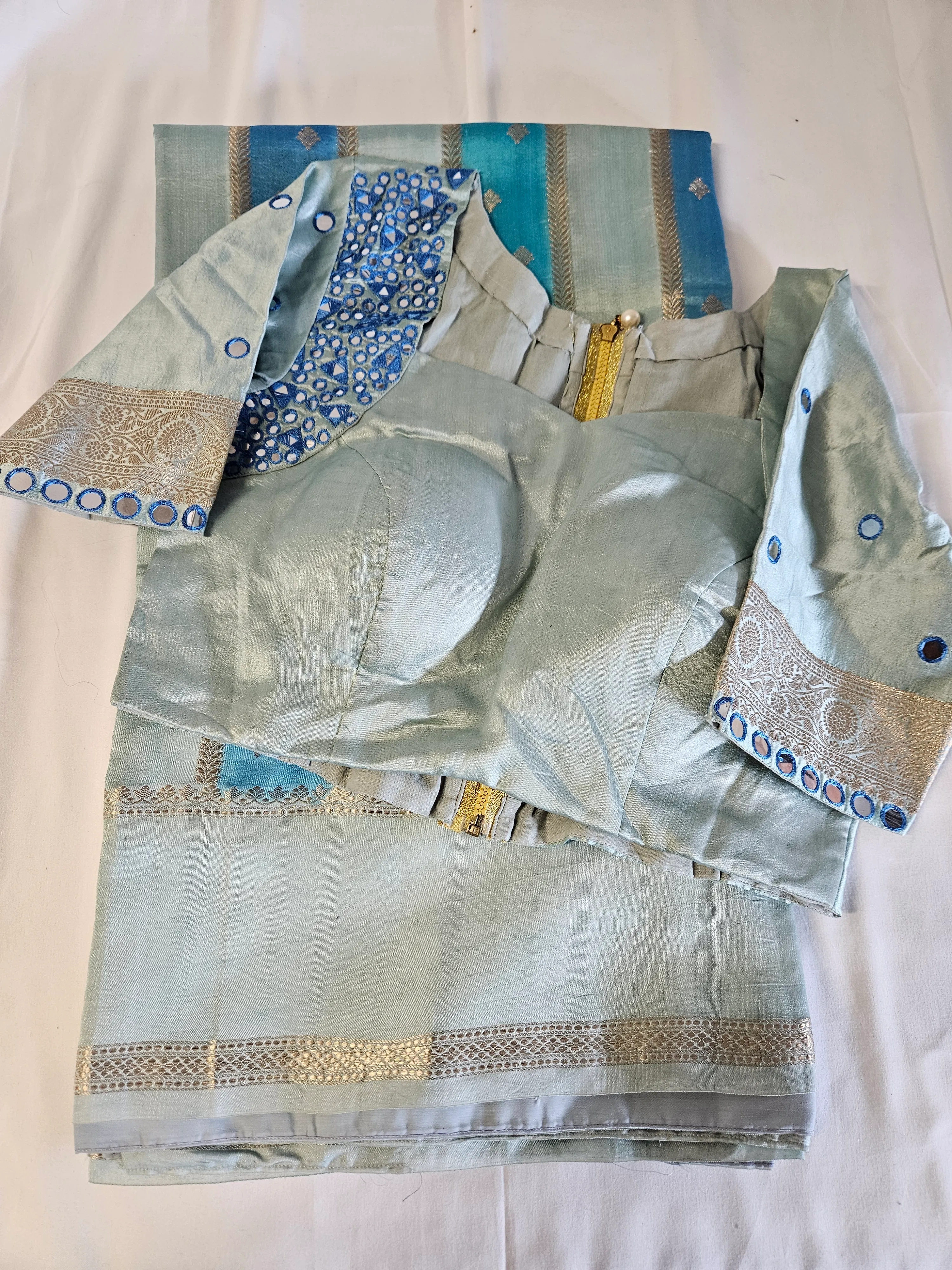 Light blue handwoven silk saree with gold zari border, paired with matching blouse featuring blue sequin embroidery and gold accents.