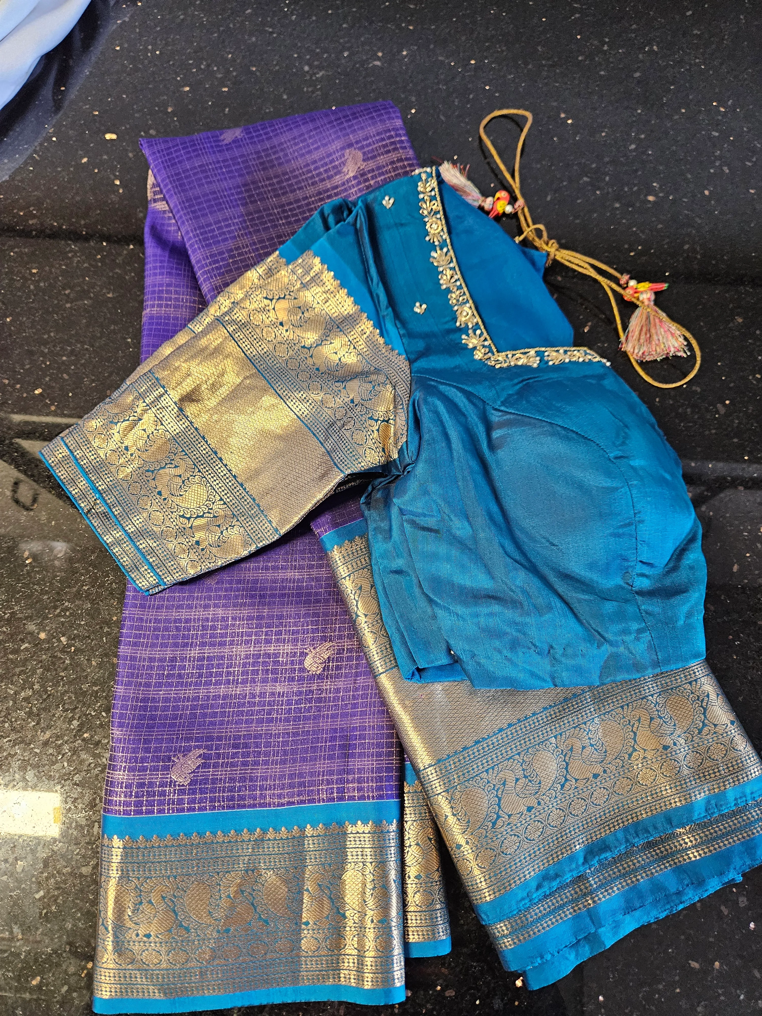 Handwoven pure Kanchipuram silk wedding saree in deep purple with gold zari border, paired with teal blue blouse featuring gold embroidery.