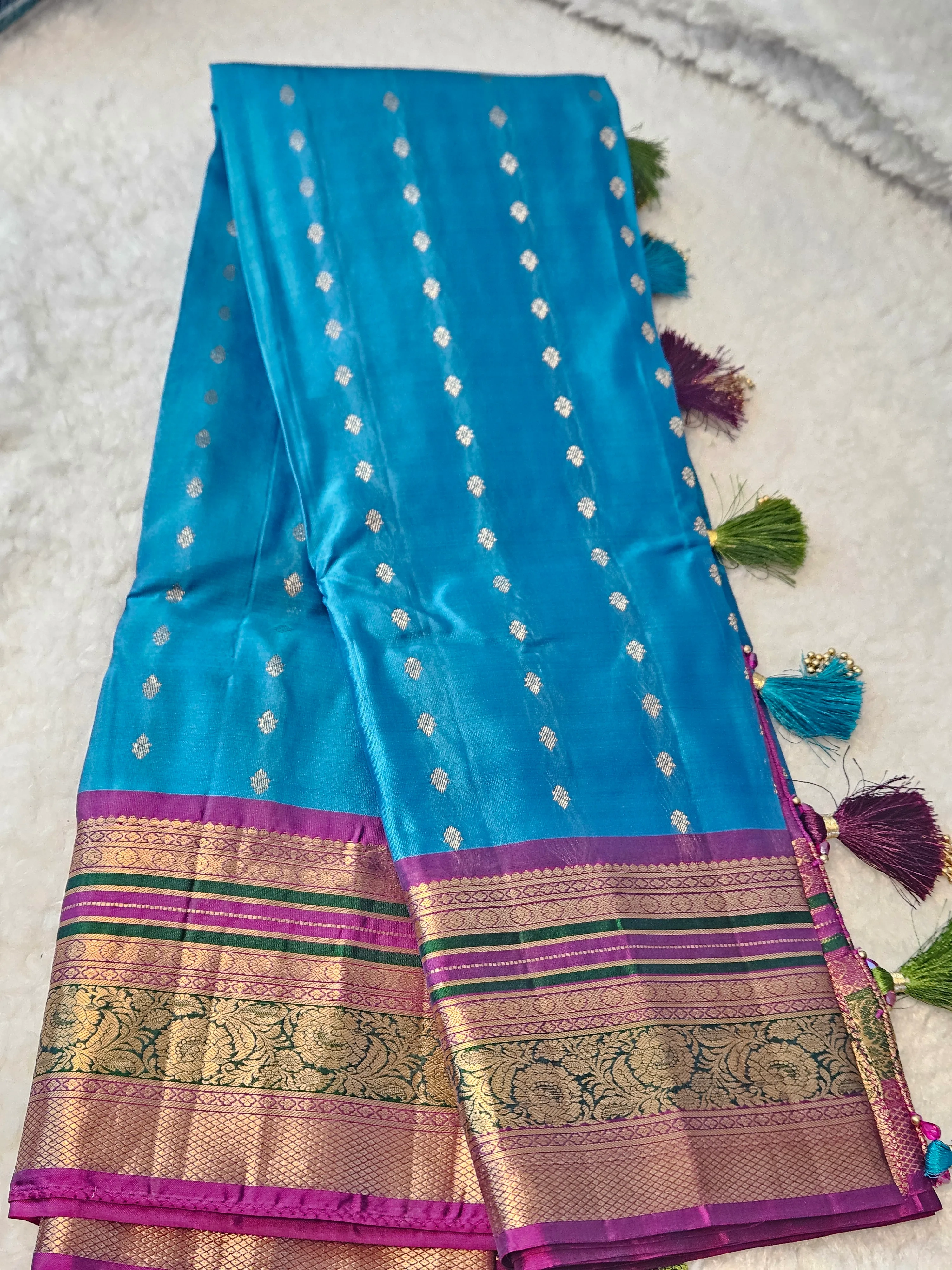 Handwoven Kanchipuram pure silk saree in vibrant blue with gold zari motifs, rich pink and green border, and silk tassels