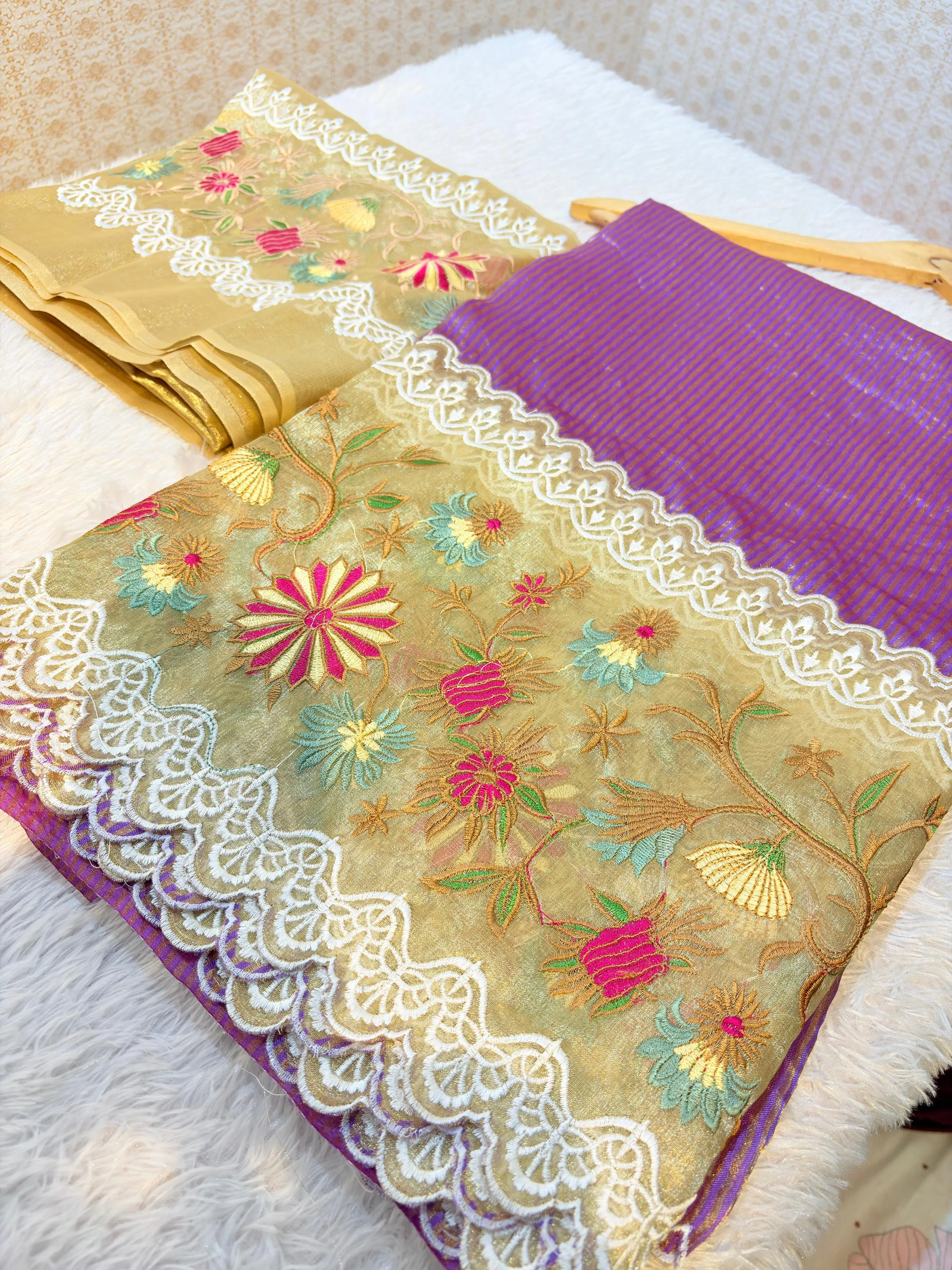 Handwoven Banarasi Kora tissue silk saree in gold with colorful floral embroidery, white lace border, and purple pallu.