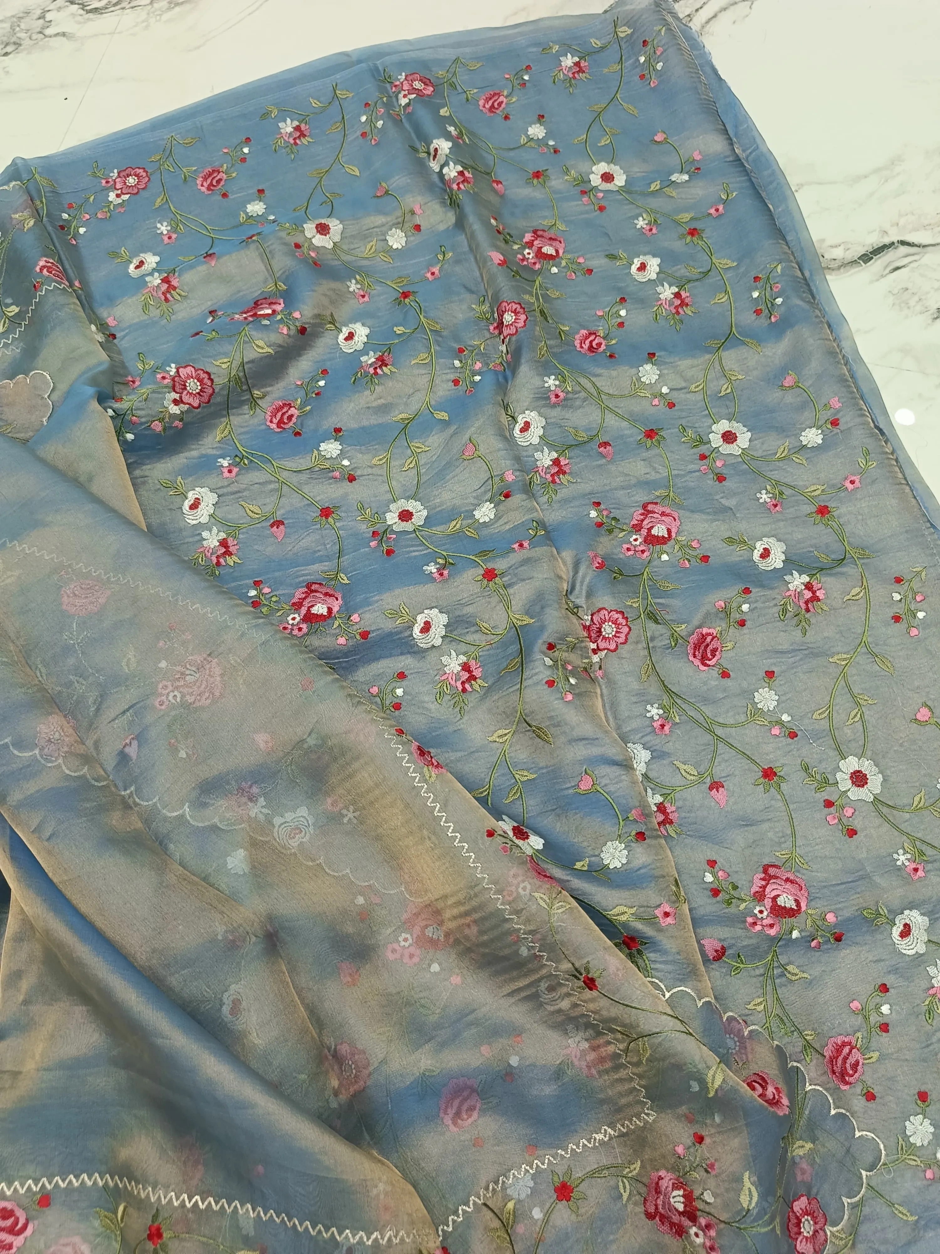 Handwoven Banarasi tissue silk saree in soft blue with gold and silver zari, featuring pink floral embroidery and delicate vines.