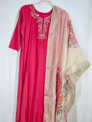 Ivory muslin Anarkali gown with intricate embroidery, paired with a beige floral dupatta, perfect for weddings and parties.